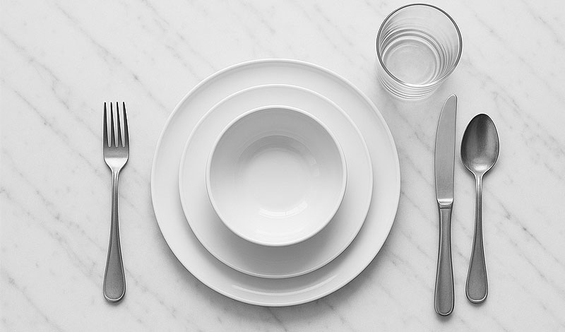 Een compleet couvert met groot bord klein bord kom glas en volledig bestekset