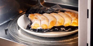 Kwetsbaar gebak op bord dat langzaam wordt opgewarmd in magnetron op 100 tot 300 watt voor delicate gerechten