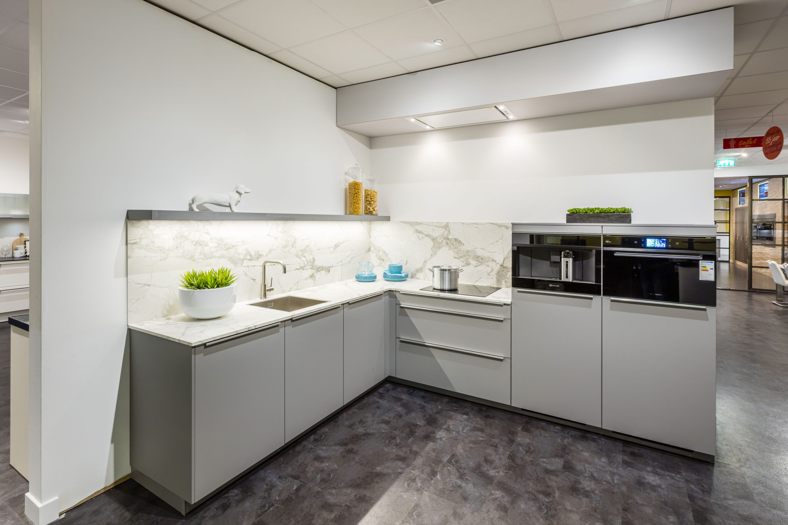 Lichtgrijze hoekkeuken met kunststof aanrechtblad en achterwand in marmer print