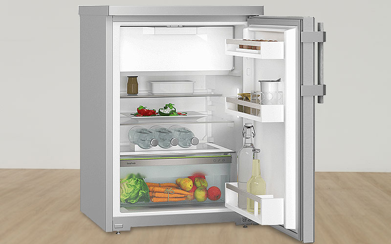 Binnenkant van een tafelmodel koelkast met groentelade, flessenrek en verstelbare glasplateaus.