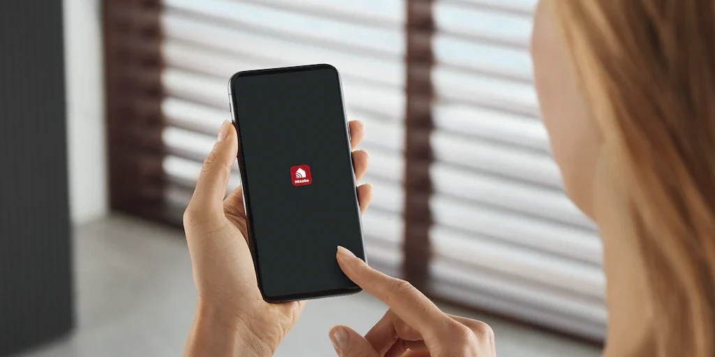 Een vrouw bediend de Miele@home app op een telefoon.