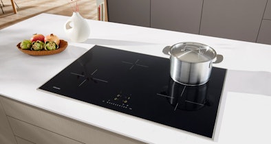 Miele inductiekookplaat met 4 afzonderlijke kookzones en een pan op het kookoppervlak in een witte keuken