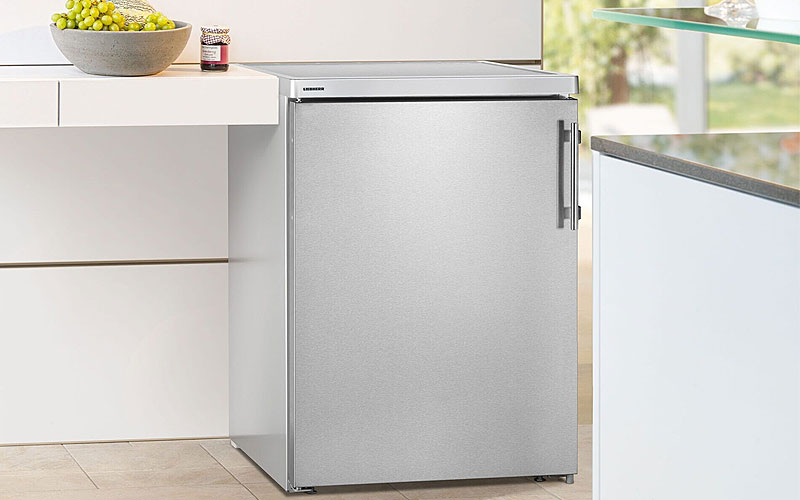 Vrijstaande tafelmodel koelkast van roestvrij staal geplaatst in moderne keuken, goed geventileerd naast werkblad.