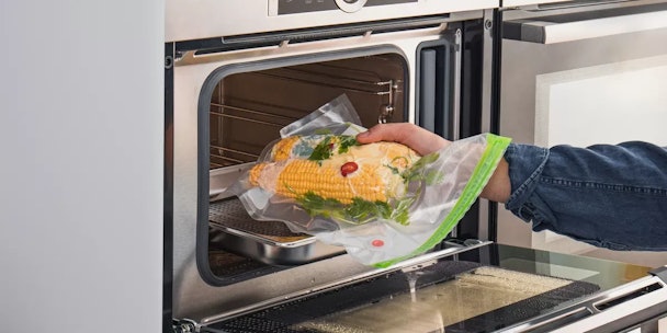 Twee vacuümverpakte maïskolven worden in de oven gelegd in om sous-vide te bereiden.