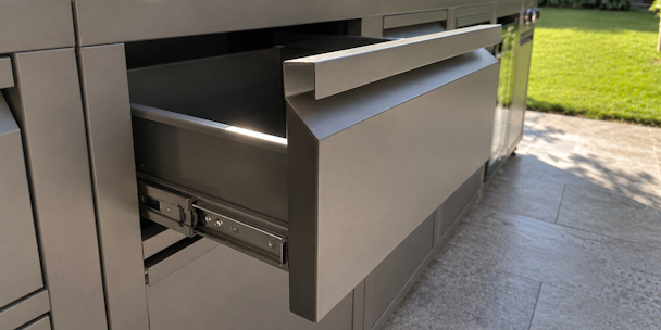 Grijze buitenkeuken met een deels geopende soft-close lade in een zonnige tuin.