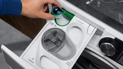 Hand plaatst een wascapsule in het groene podsvak van de AEG UniversalDose-wasmiddellade.
