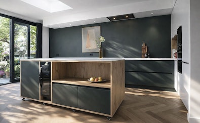 Verrijdbaar keukeneiland op wielen met open vakken en donkere kastdeurtjes in een moderne keuken met donkergroene muur