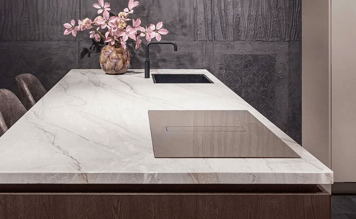 Wave Peyto inductiekookplaat met afzuiging in Smoked Silver, vlak ingebouwd in een wit marmeren werkblad op een kookeiland