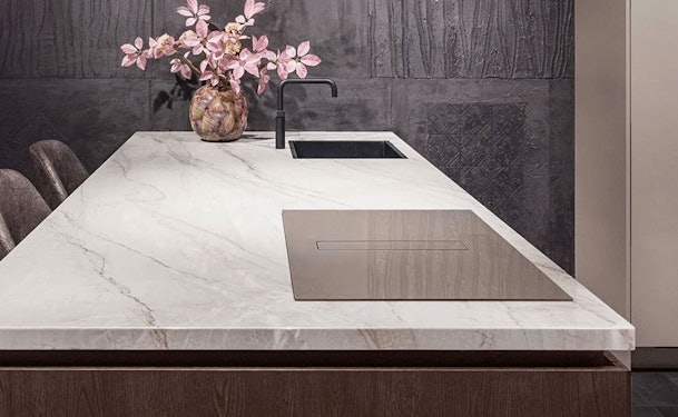 Wave Peyto inductiekookplaat met afzuiging in Smoked Silver, vlak ingebouwd in een wit marmeren werkblad op een kookeiland