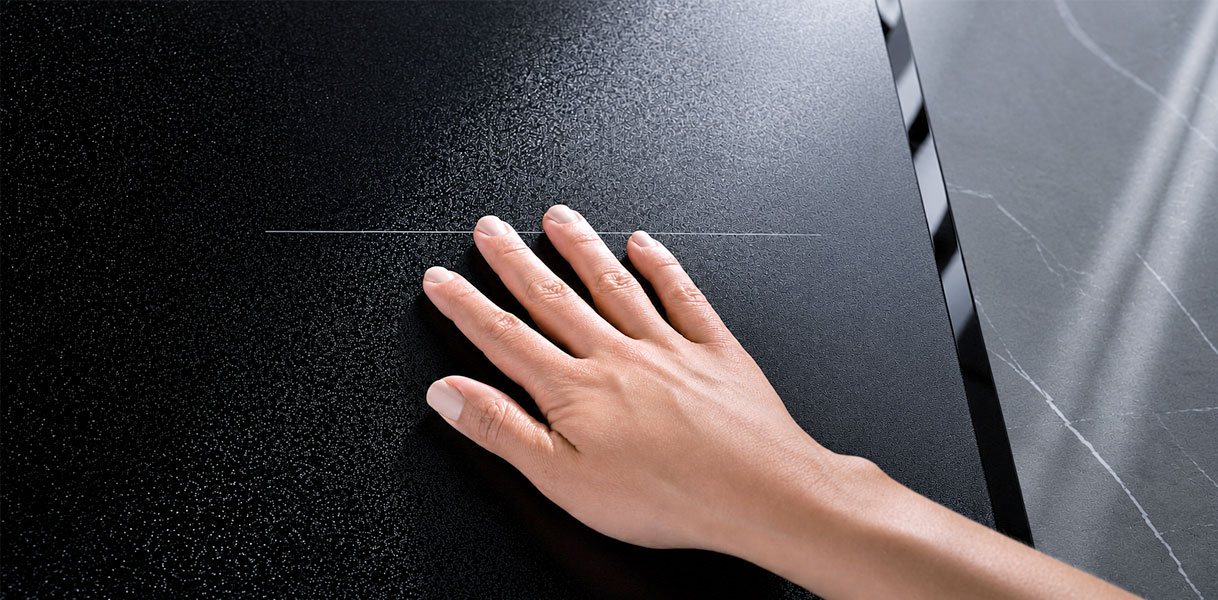 Hand strijkt over het matte glas van een AEG kookplaat in het werkblad