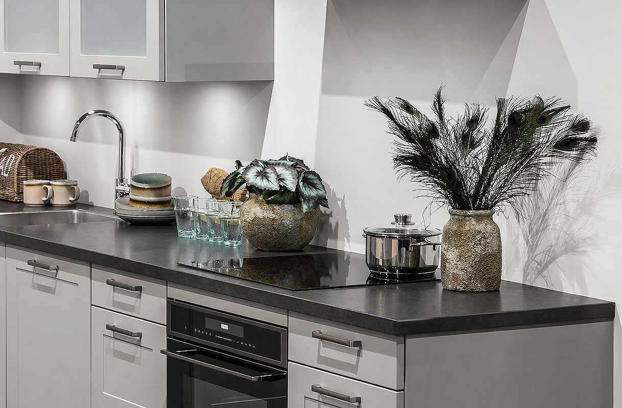 Rechte keuken met inbouwoven, kookplaat, spoelbak en decoratie met pauwenveren en plant