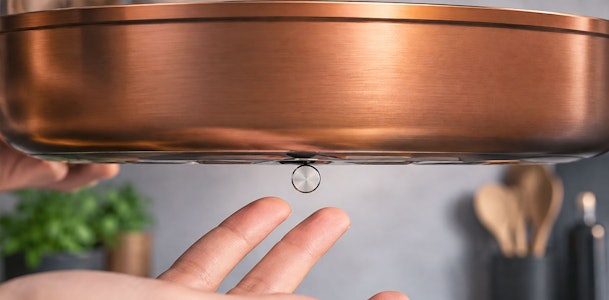 Hand houdt een magneet tegen de bodem van een koperen pan als geschiktheidstest