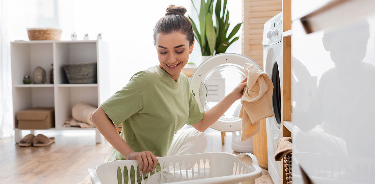 Vrouw haalt tevreden de was uit haar wasmachine in een lichte bijkeuken
