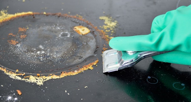 Aangekoekte etensresten van inductie kookplaat verwijderen met kookplaatschraper