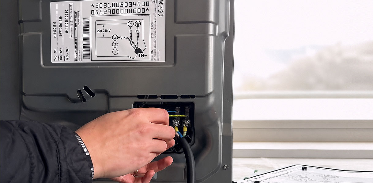 Hand sluit de aansluitkabel aan op de achterkant van een oven met typeplaatje erboven