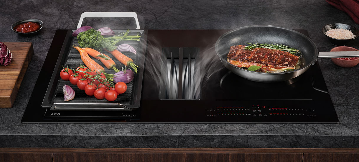 AEG inductiekookplaat met geïntegreerde afzuiging zuigt kookdampen weg tussen een grillplaat met groenten en een pan met vlees