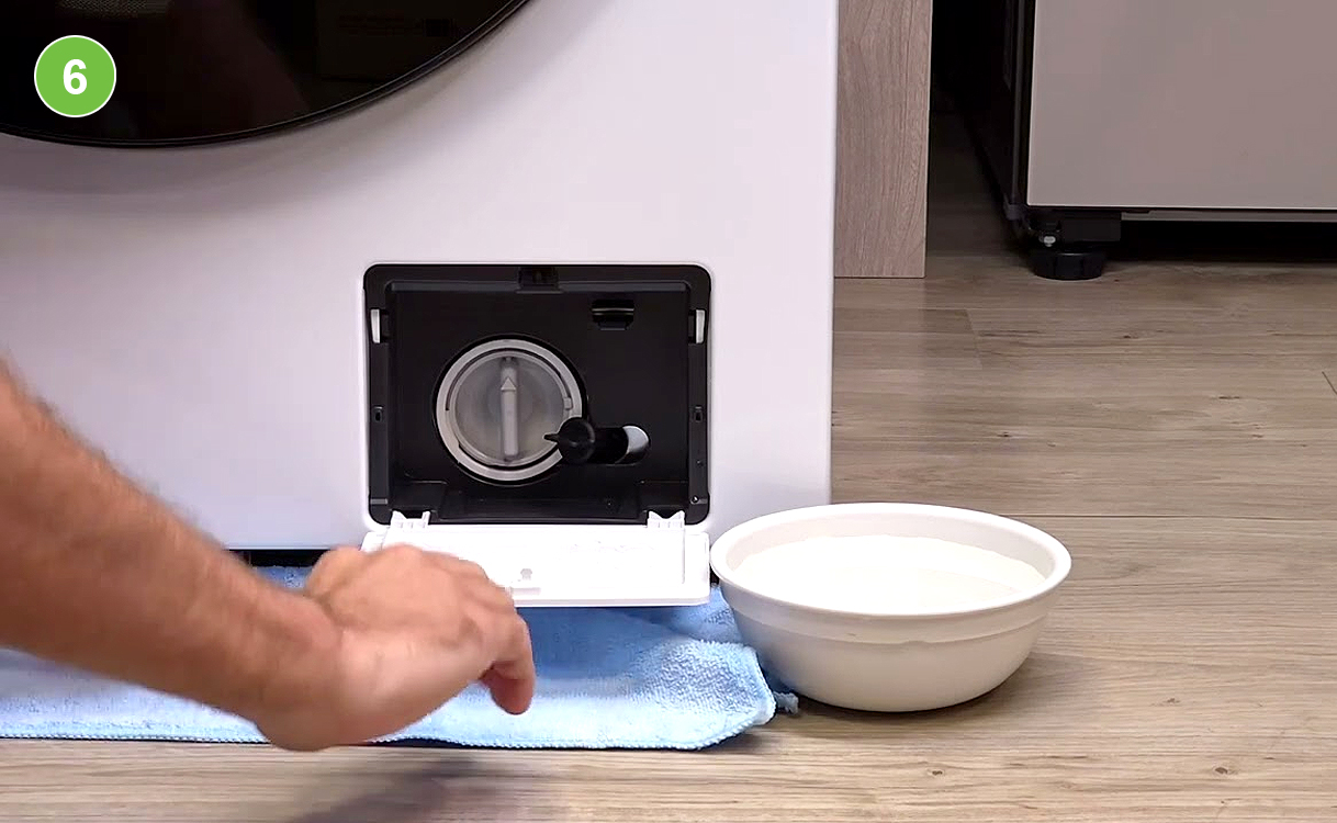 Afvoerfilter van een wasmachine wordt geleegd met handdoek en opvangbak