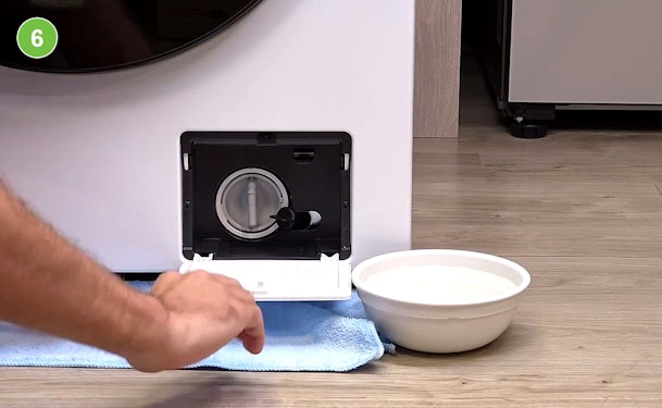 Afvoerfilter van een wasmachine wordt geleegd met handdoek en opvangbak