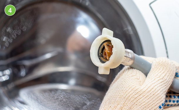 Afvoerslang van een wasmachine losgehaald met zichtbaar vuil en restwater in de slang