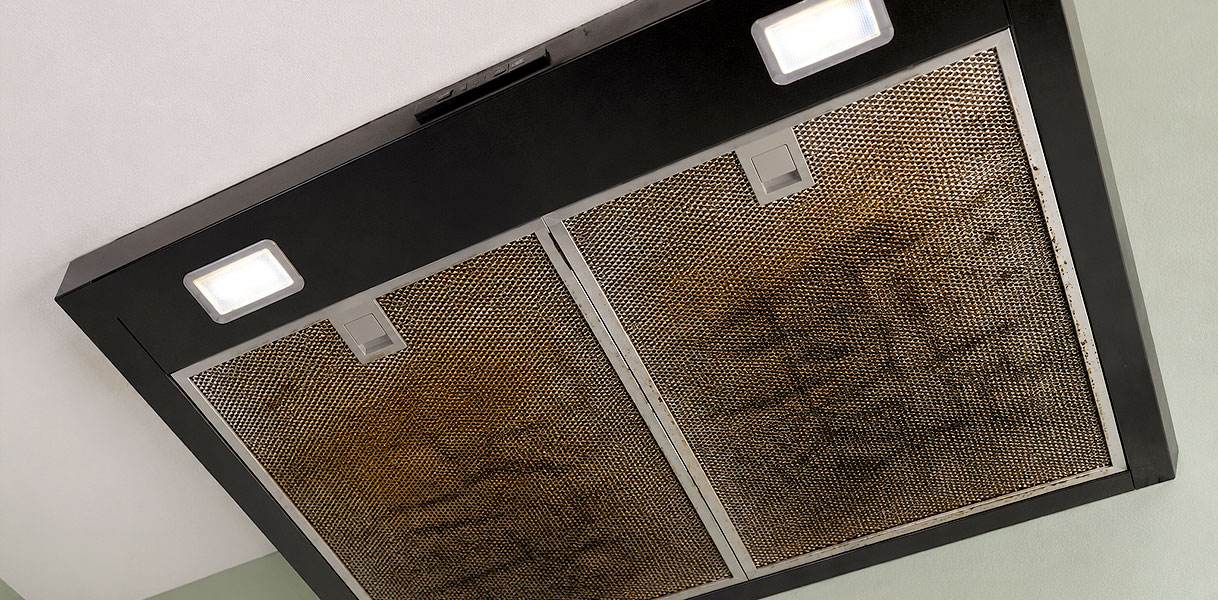 Vervuilde metalen vetfilters in een onderbouw afzuigkap met ingeschakelde verlichting