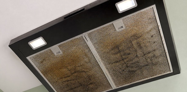 Vervuilde metalen vetfilters in een onderbouw afzuigkap met ingeschakelde verlichting
