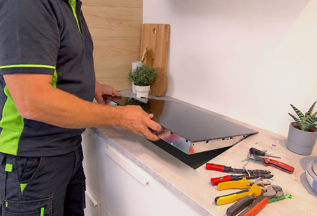 Installateur plaatst een inductiekookplaat in de uitsparing van het werkblad met gereedschap ernaast