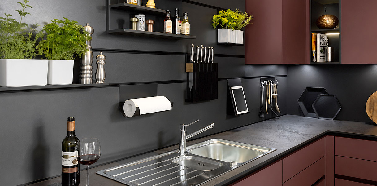 Bordeauxrode keuken met donkere achterwand, RVS spoelbak en kruidenplankjes met accessoires