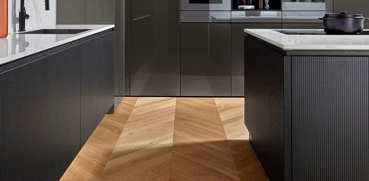 Moderne keuken met antracietkleurige fronten en wit composiet werkblad, gecombineerd met een warme houten visgraatvloer voor een strak en luxe contrast.