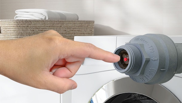 Vinger drukt rood pinnetje in Aquastop-connector van wasmachine waterslang om te resetten