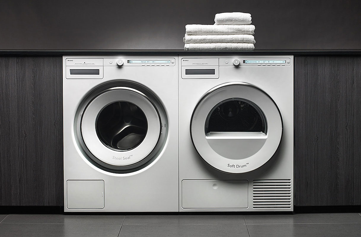 Asko wasmachine en droger naast elkaar met opgevouwen handdoeken bovenop in moderne wasruimte