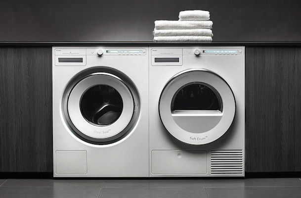 Asko wasmachine en droger naast elkaar met opgevouwen handdoeken bovenop in moderne wasruimte