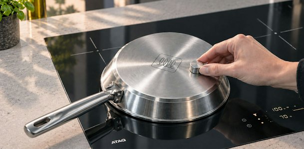 Hand houdt een magneet tegen de bodem van een pan op een ATAG kookplaat