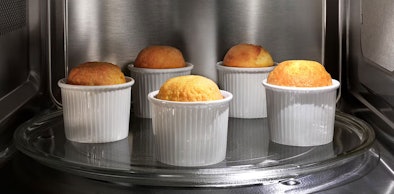 Vijf soufflés in witte ramekins die gelijkmatig garen in Electrolux magnetron via automatisch kookprogramma