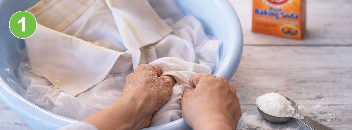 Witte was weken in baking soda: handen kneden wit textiel in een teiltje met water, baking soda en maatlepel op de achtergrond