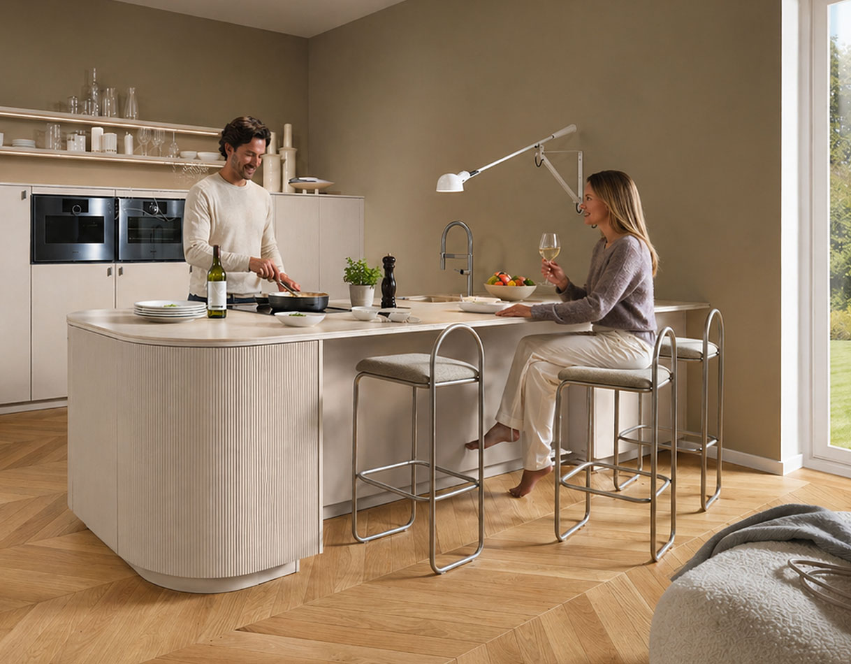 Kookeiland met bar en zitplaatsen, vrouw drinkt wijn terwijl man kookt in moderne open keuken.