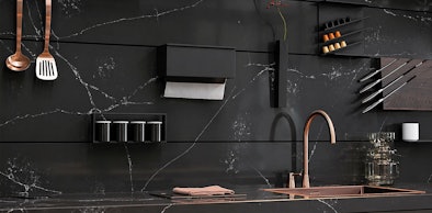 Marmerlook achterwand met magnetische messenstrip, kookgerei, wandrekken en koperen kraan boven spoelbak