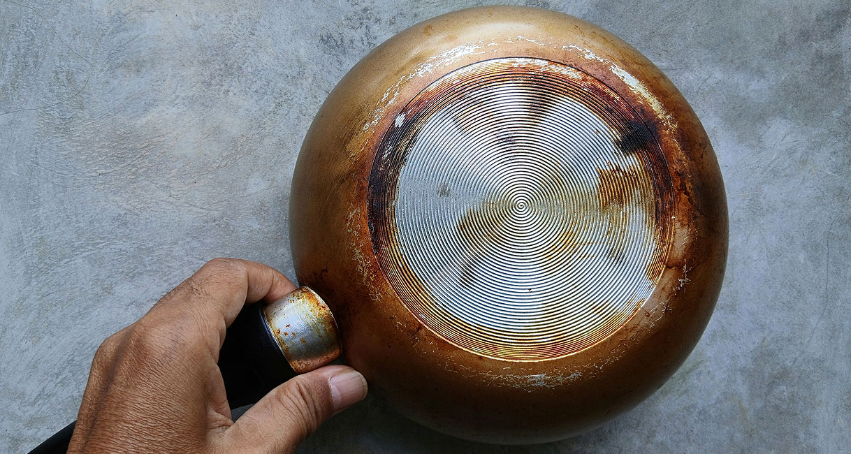 Hand houdt pan ondersteboven om beschadigde bodem te controleren voor gebruik op inductie