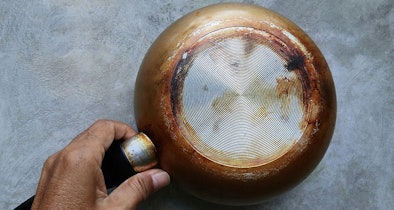 Hand houdt pan ondersteboven om beschadigde bodem te controleren voor gebruik op inductie