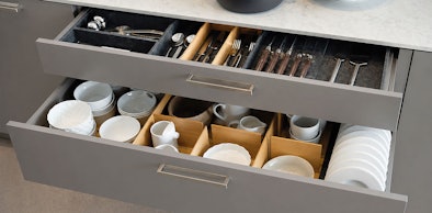 Twee geopende keukenlades met bestekvak en houten indelingen voor borden, kommen en kopjes