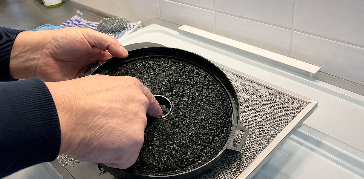 Handen plaatsen een koolstoffilter terug in de vetfilter van een recirculatie afzuigkap