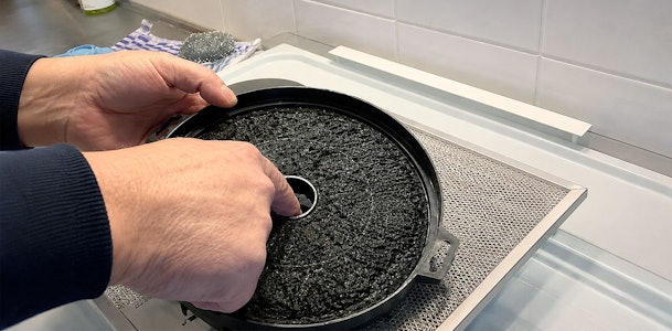 Handen plaatsen een koolstoffilter terug in de vetfilter van een recirculatie afzuigkap