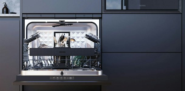 Geopende BORA Dish vaatwasser op werkhoogte in een donkere keuken, met verlichte binnenruimte en een gevulde vaatwasserkorf met servies, glazen en bestek.