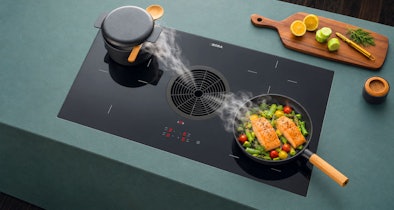 BORA keramische kookplaat met afzuiging en koekenpan met groenten naast gietijzeren pan op werkblad