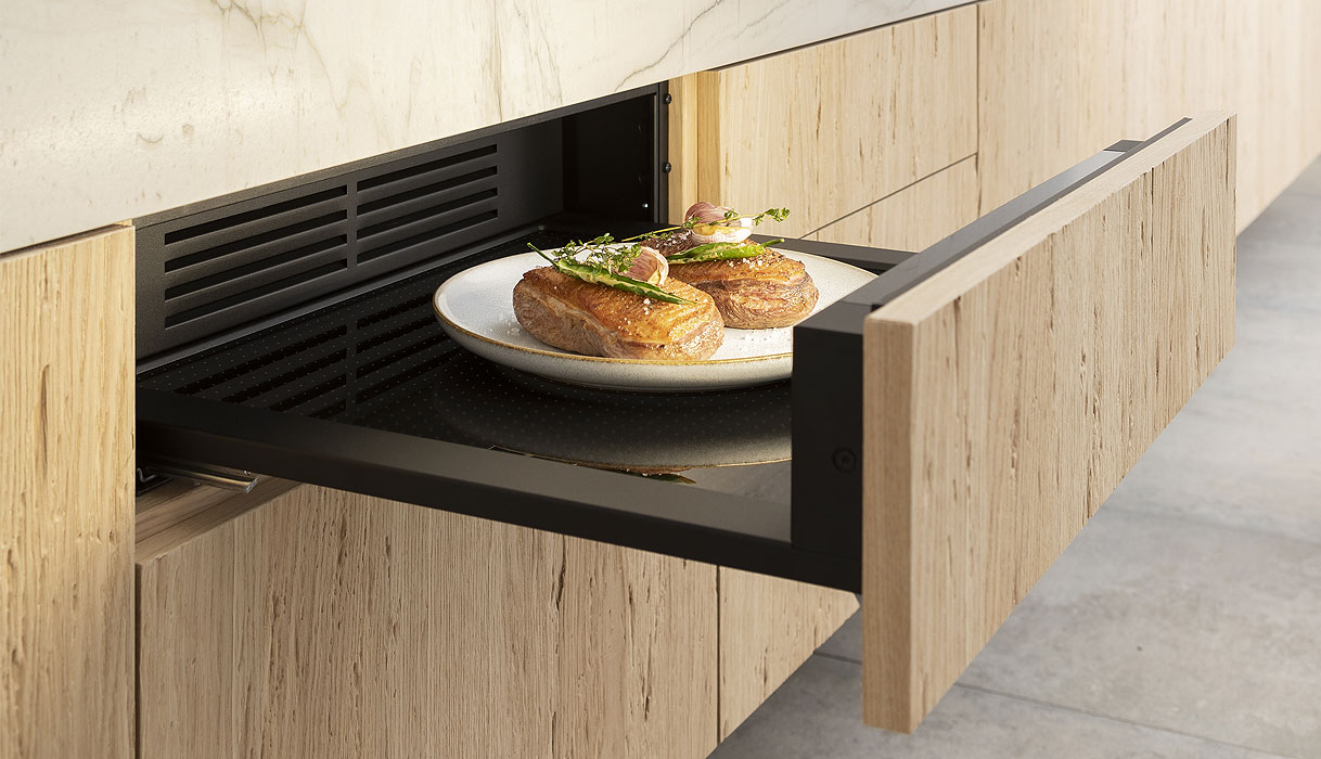 Geopende BORA multifunctionele lade met houten keukenfront, ingebouwd onder een marmeren werkblad, met een bord met twee opgemaakte gerechten.