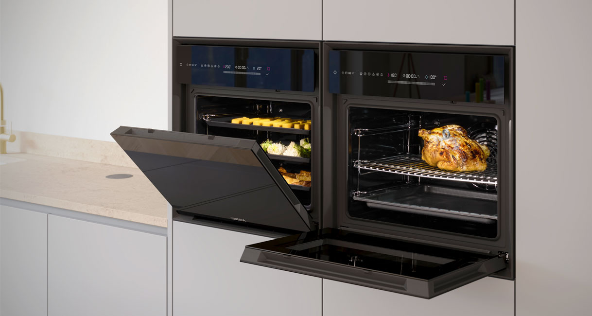 Twee BORA Oven Steam stoomovens met geopende deuren in een moderne keuken, met links gerechten op drie bakniveaus en rechts een gebraden kip.