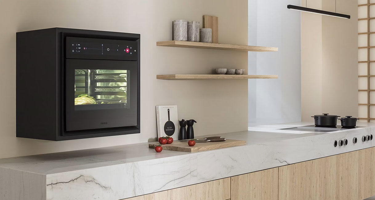 BORA X BO stoomoven ingebouwd in een moderne keuken met marmeren werkblad, lichte houten keukenkasten en een gerecht achter het ovenvenster.