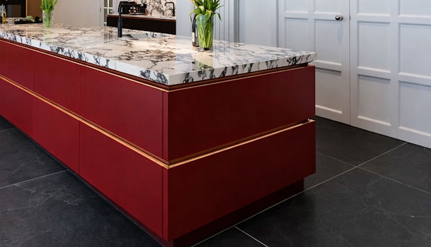 Bordeauxrood kookeiland met marmerlook werkblad en goudkleurige accenten in moderne open keuken.