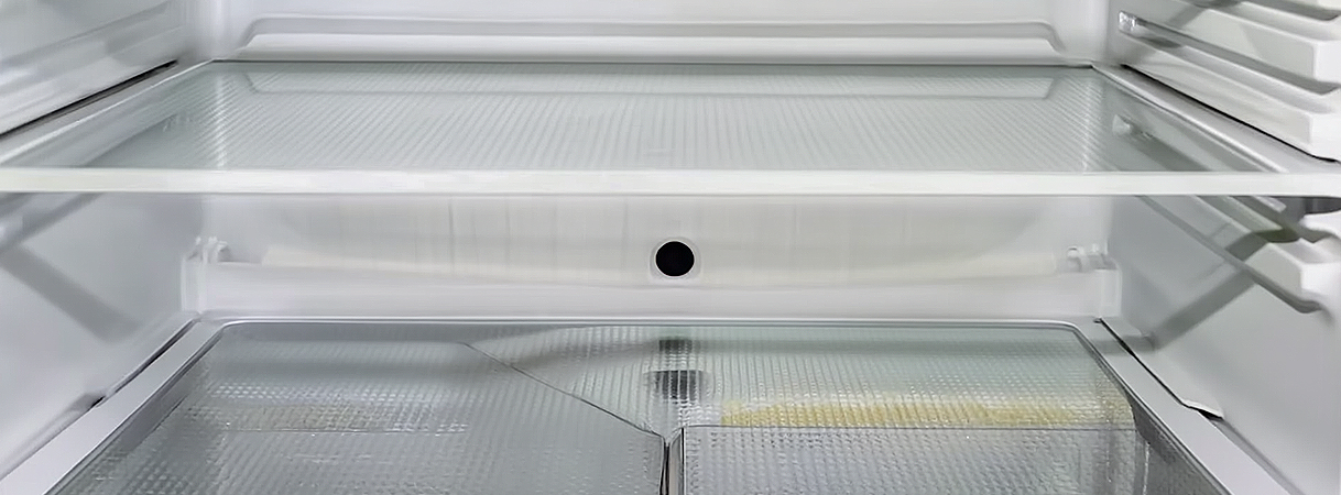 Binnenkant van een koelkast met condens en het afvoergaatje zichtbaar.