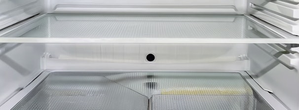 Binnenkant van een koelkast met condens en het afvoergaatje zichtbaar.