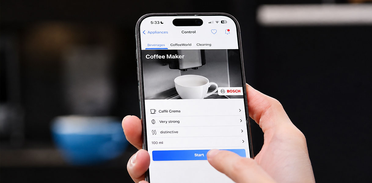 Hand bedient een Bosch koffiemachine op afstand via de Home Connect app op een telefoon